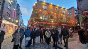 Grupo de estudiantes en una calle turística decorada con luces navideñas frente a The Temple Bar en Dublín, mostrando una experiencia típica de quienes buscan estudiar inglés en el extranjero.v